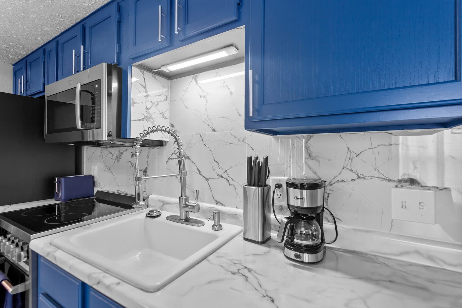 Kitchen detail with a farmhouse sink, a marble backsplash, and blue cabinets