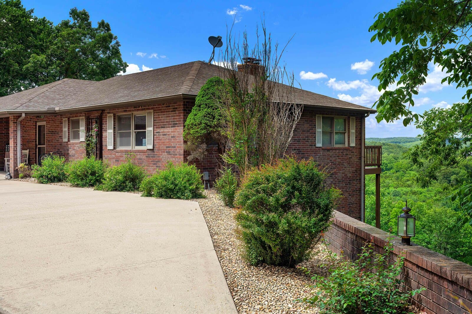 Brick home on a ridge with a driveway and a wooded Ozark valley view