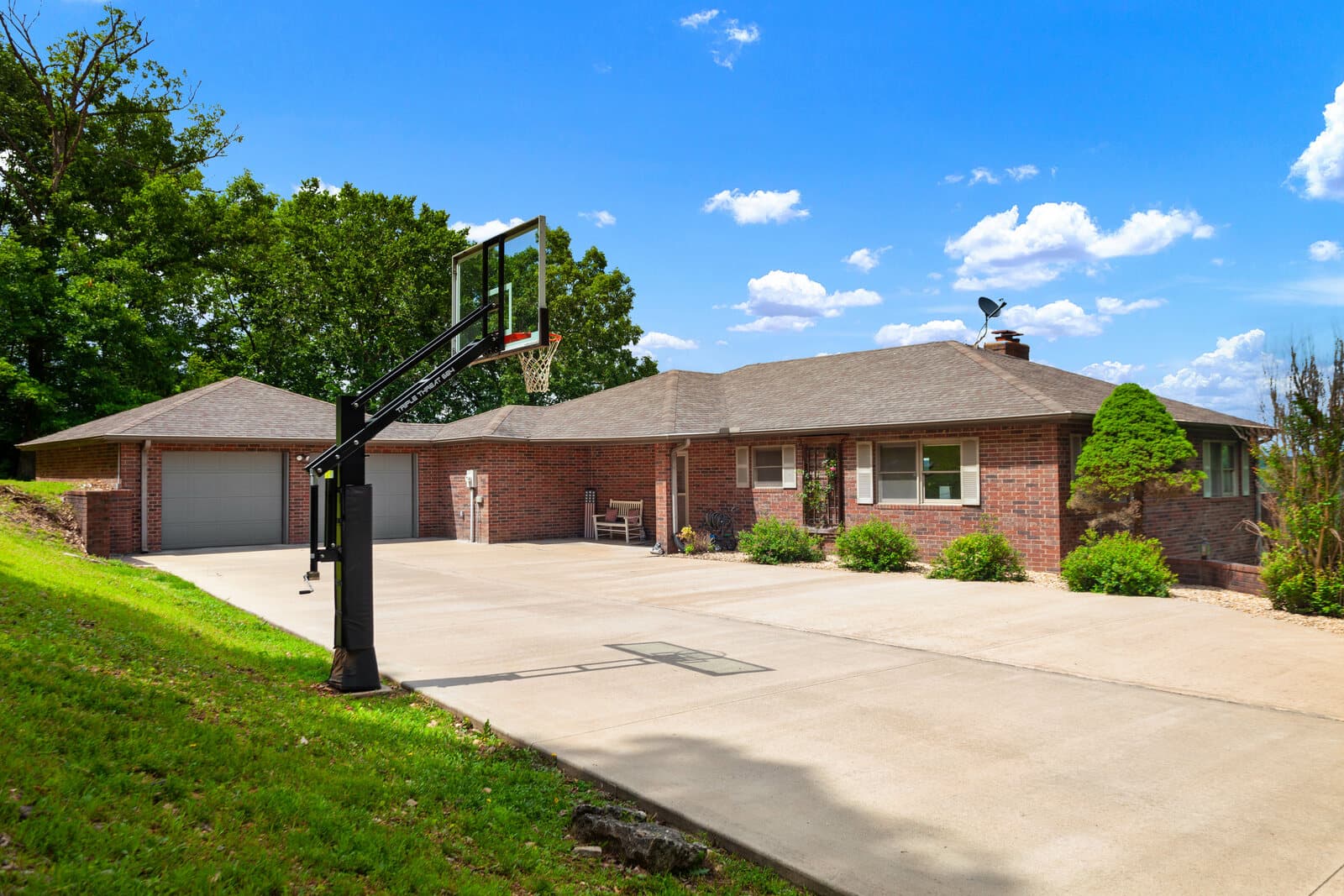 Brick ranch home with a basketball hoop and a wide concrete driveway
