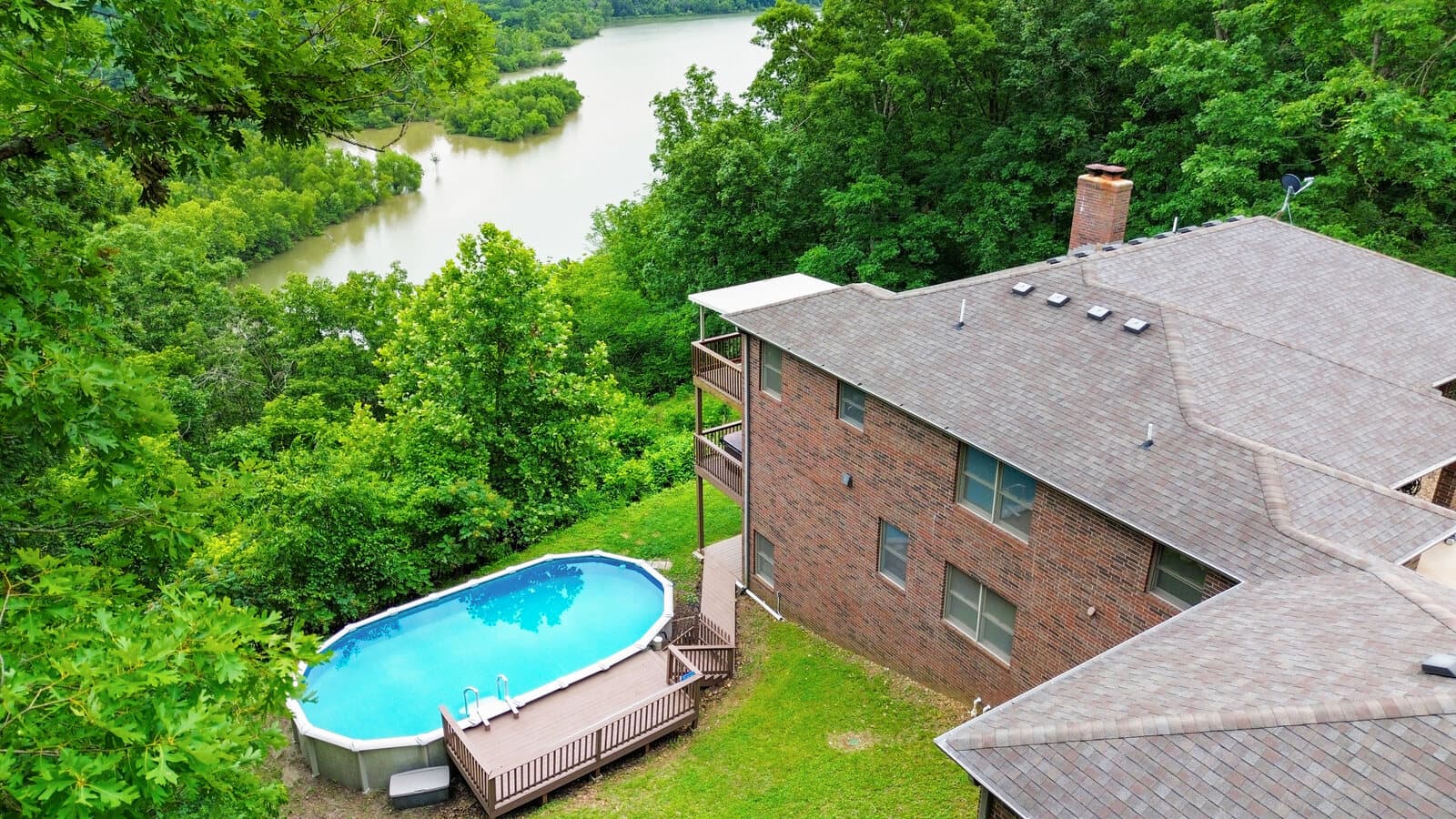 Elevated view of a hillside home with an above-ground pool and a deck above the water