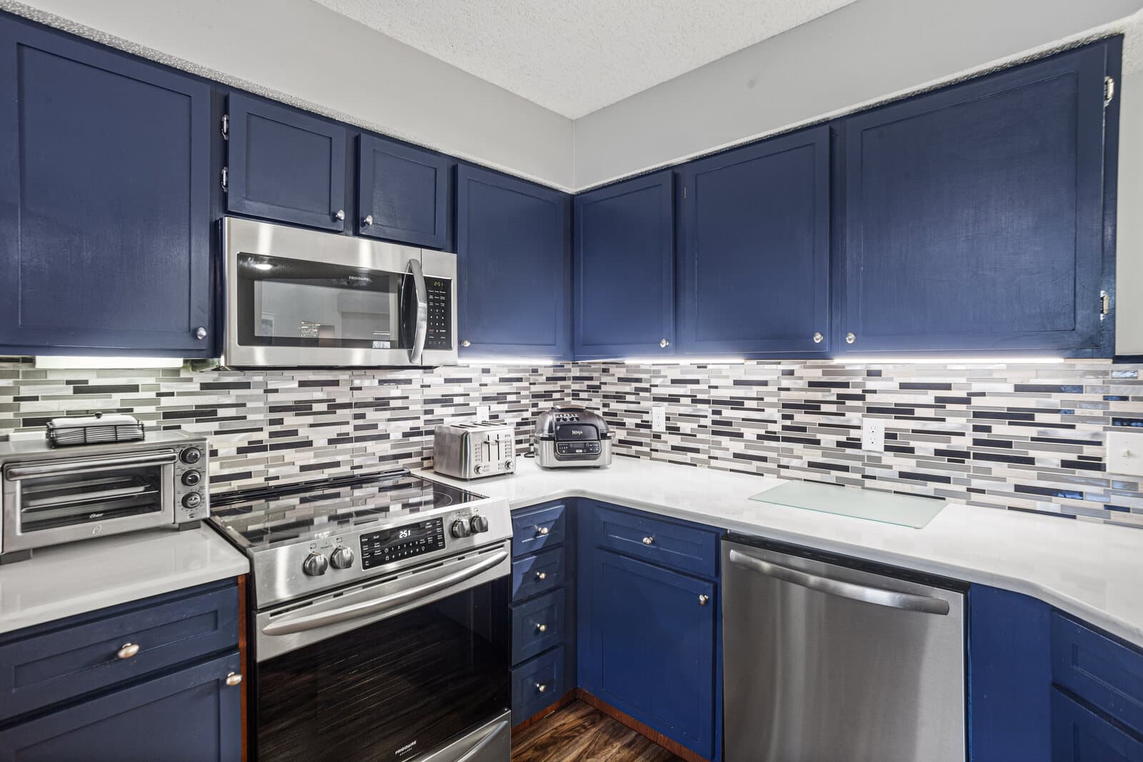 Kitchen with navy blue cabinets, stainless steel appliances, and a tile backsplash