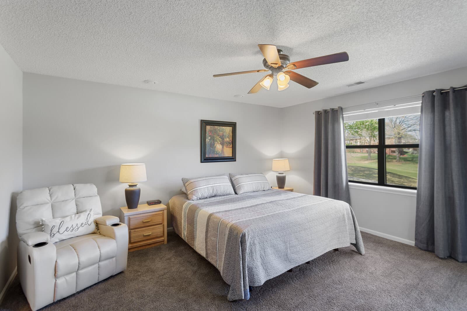 Bedroom with a king bed, a white recliner, and a window overlooking a green lawn