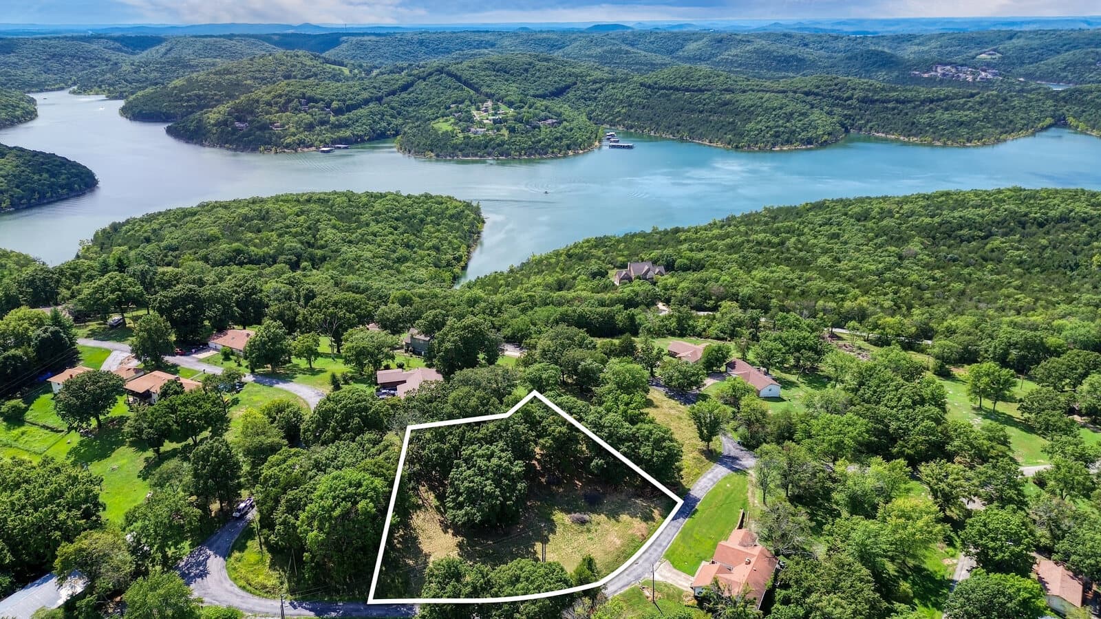 Aerial of a wooded residential lot outlined for sale above a large Ozark lake